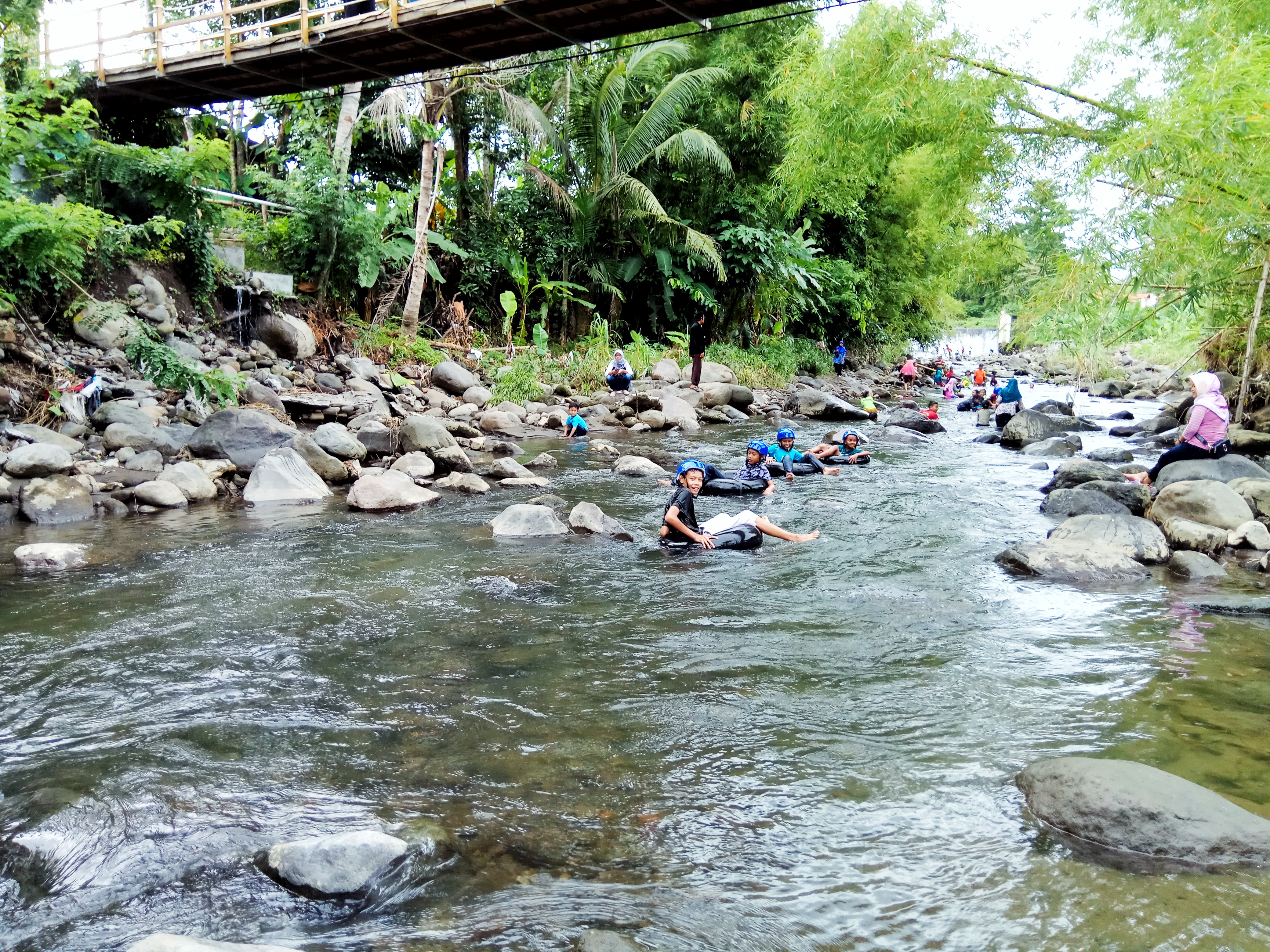 Pengunjung bermain air di sungai bawah Jembatan Goyang